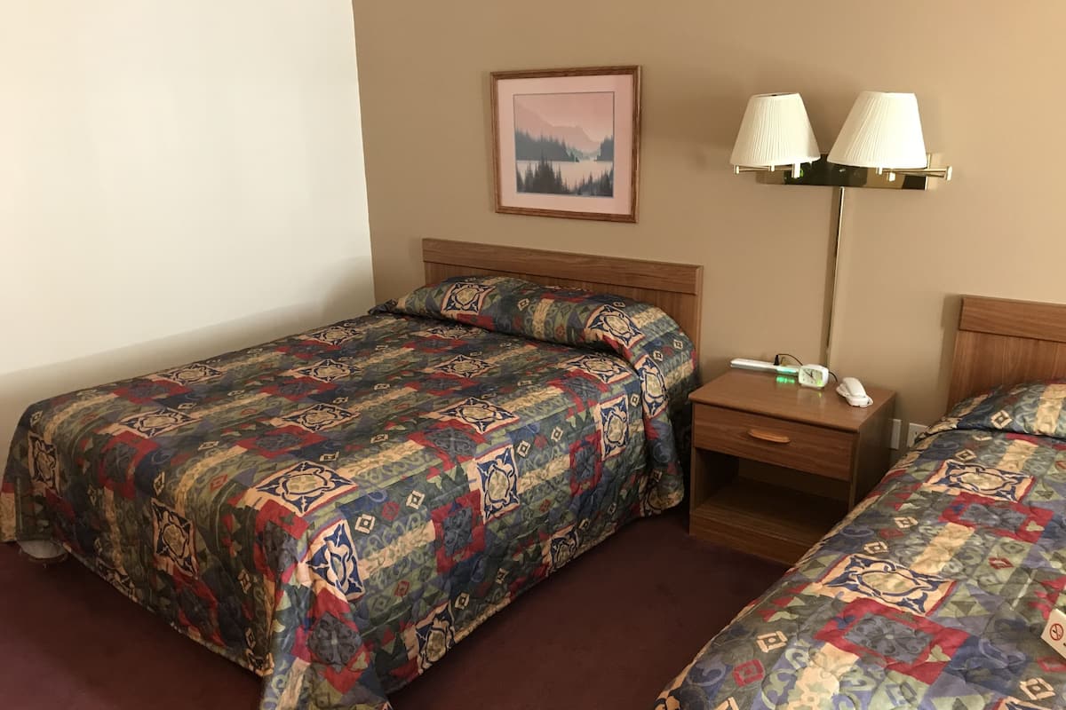 A hotel room with two single beds, a nightstand with a lamp, a framed picture on the wall, and a small table with a phone and a clock.