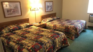 A hotel room with two beds, each with a colorful quilt, a bedside table with a lamp, and framed artwork on the walls. - Badger Motel (Chippewa Falls)