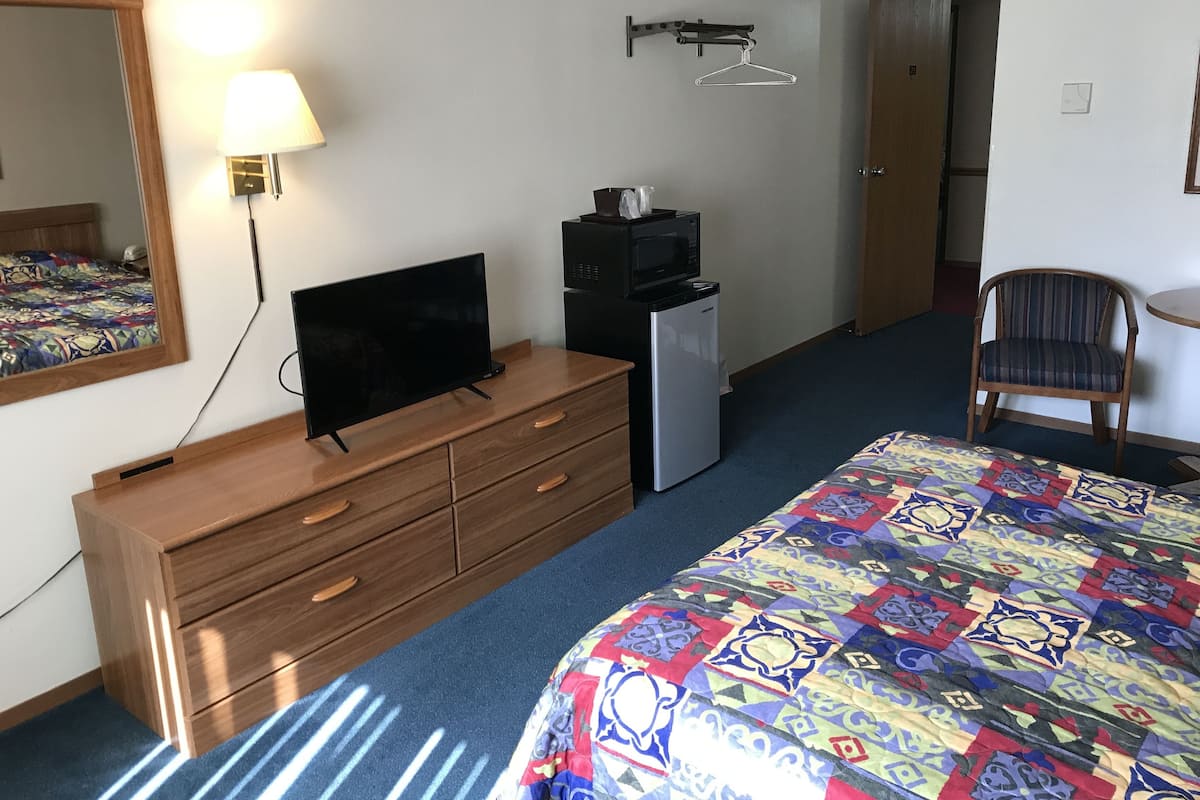 A hotel room with a bed, a dresser, a television, a microwave, and a chair.