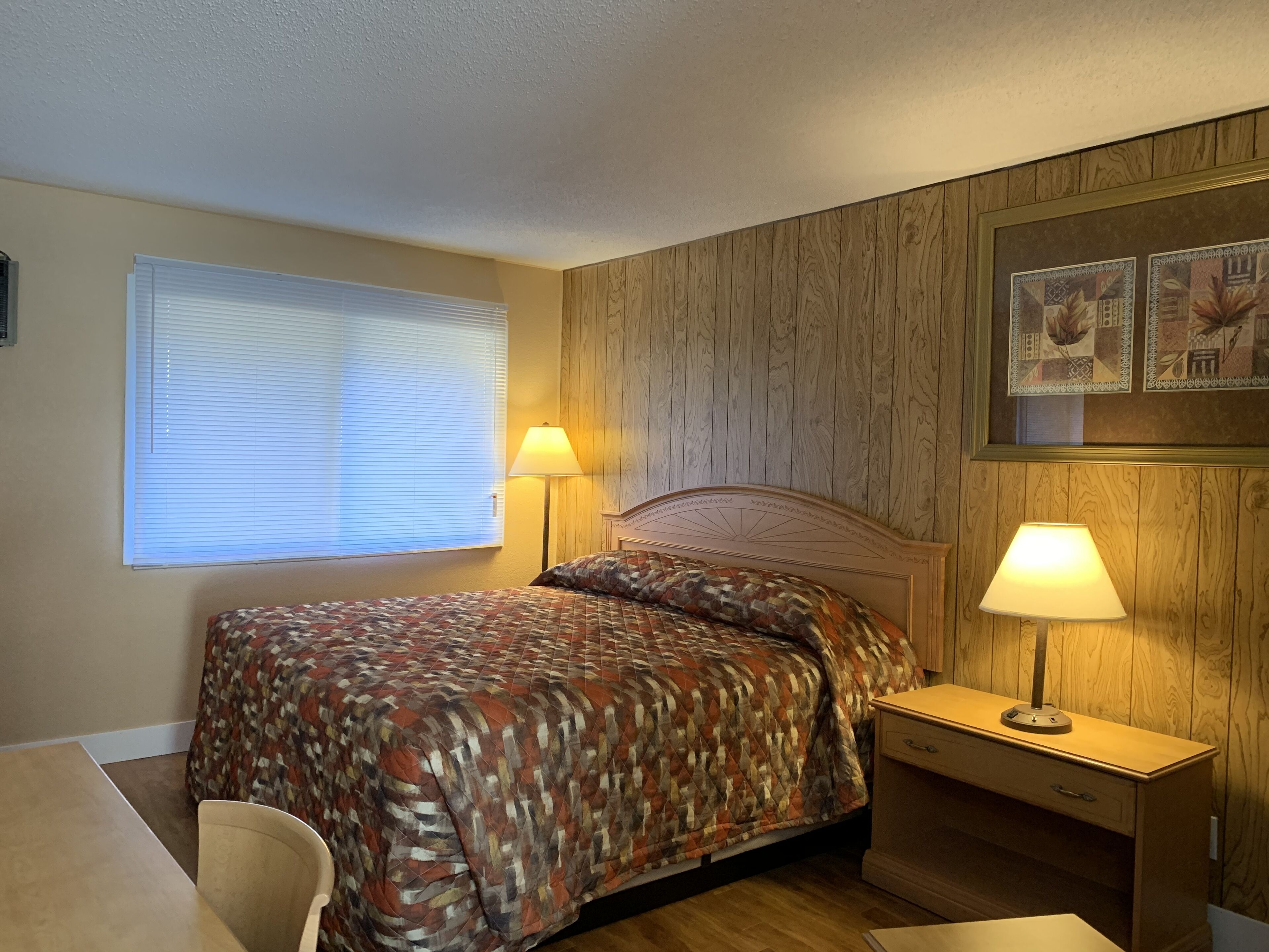 Une chambre à coucher comprenant un lit, deux lampes de chevet, une table de chevet, une chaise et une fenêtre avec des stores.
