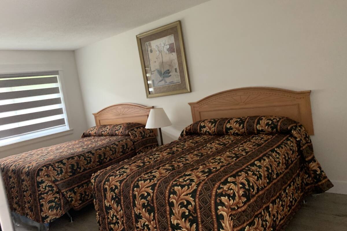 A bedroom with two beds, a nightstand, a lamp, and a framed picture on the wall.