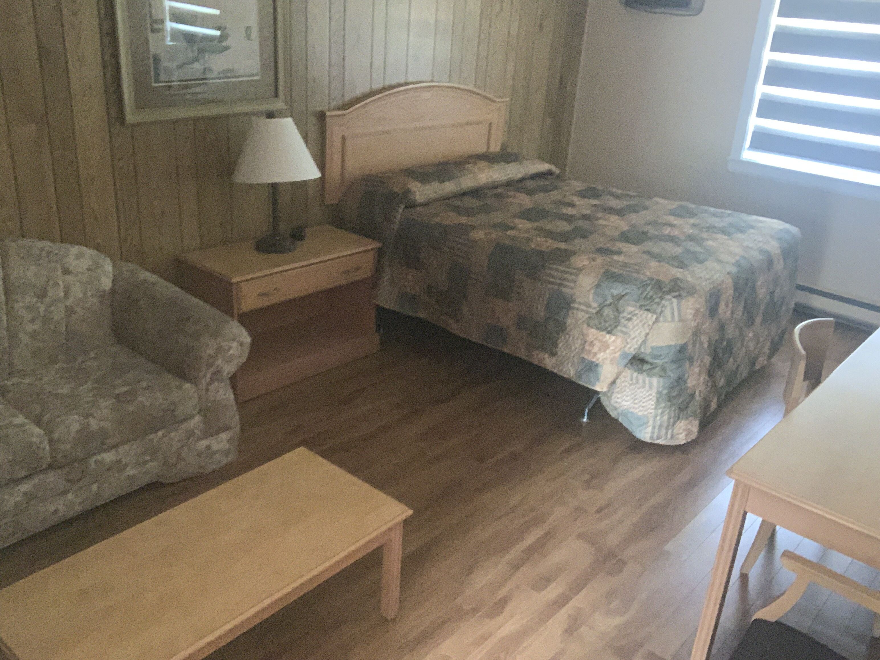 A small, cozy room with a single bed, a nightstand with a lamp, a wooden bench, and a chair.