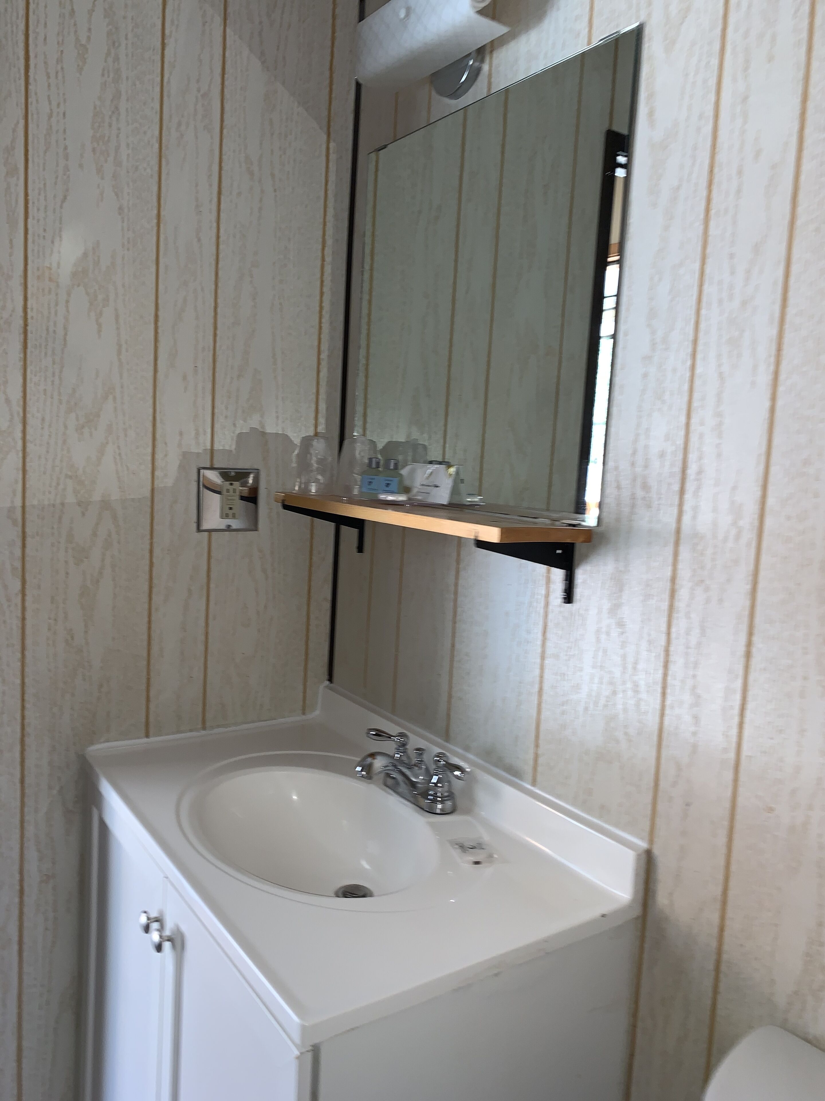 A bathroom with a white sink, a mirror, and a shelf above the sink.