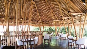 Un espacio comedor al aire libre con estructuras de bambú, mesas y sillas.