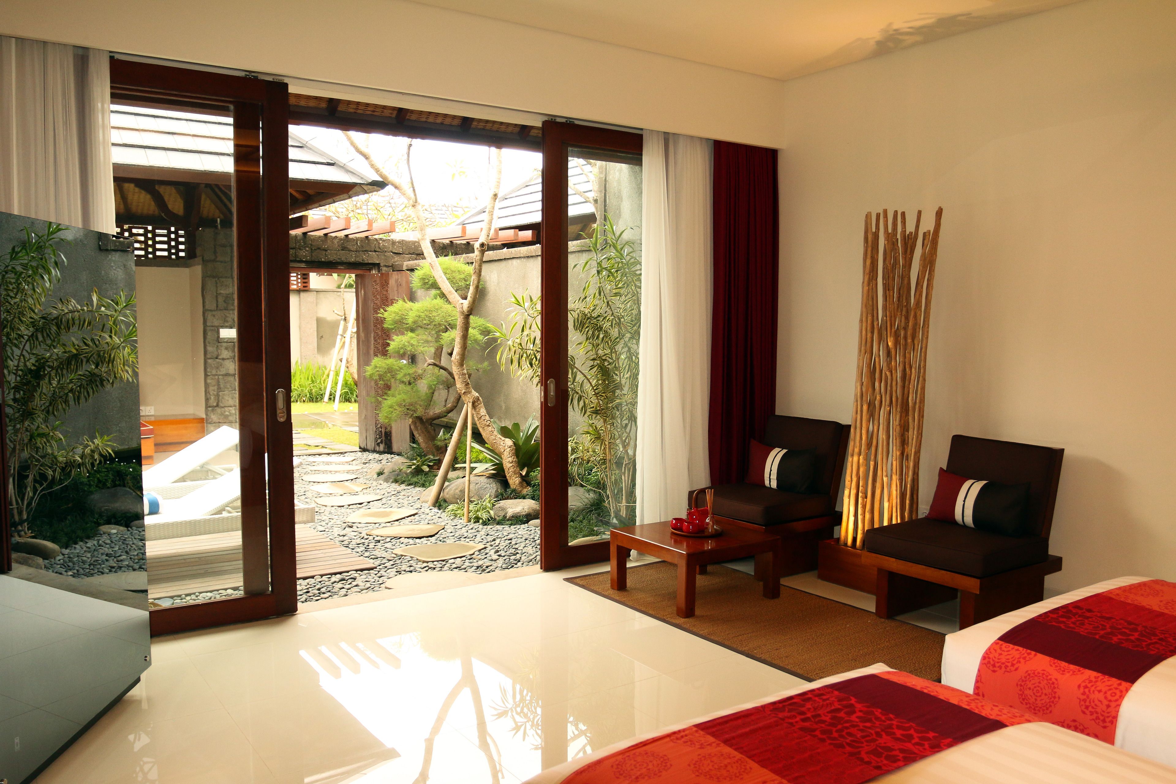 Une chambre d’hôtel moderne avec un grand lit, deux canapés, une petite table et une vue sur un jardin, accessible par une porte coulissante.
