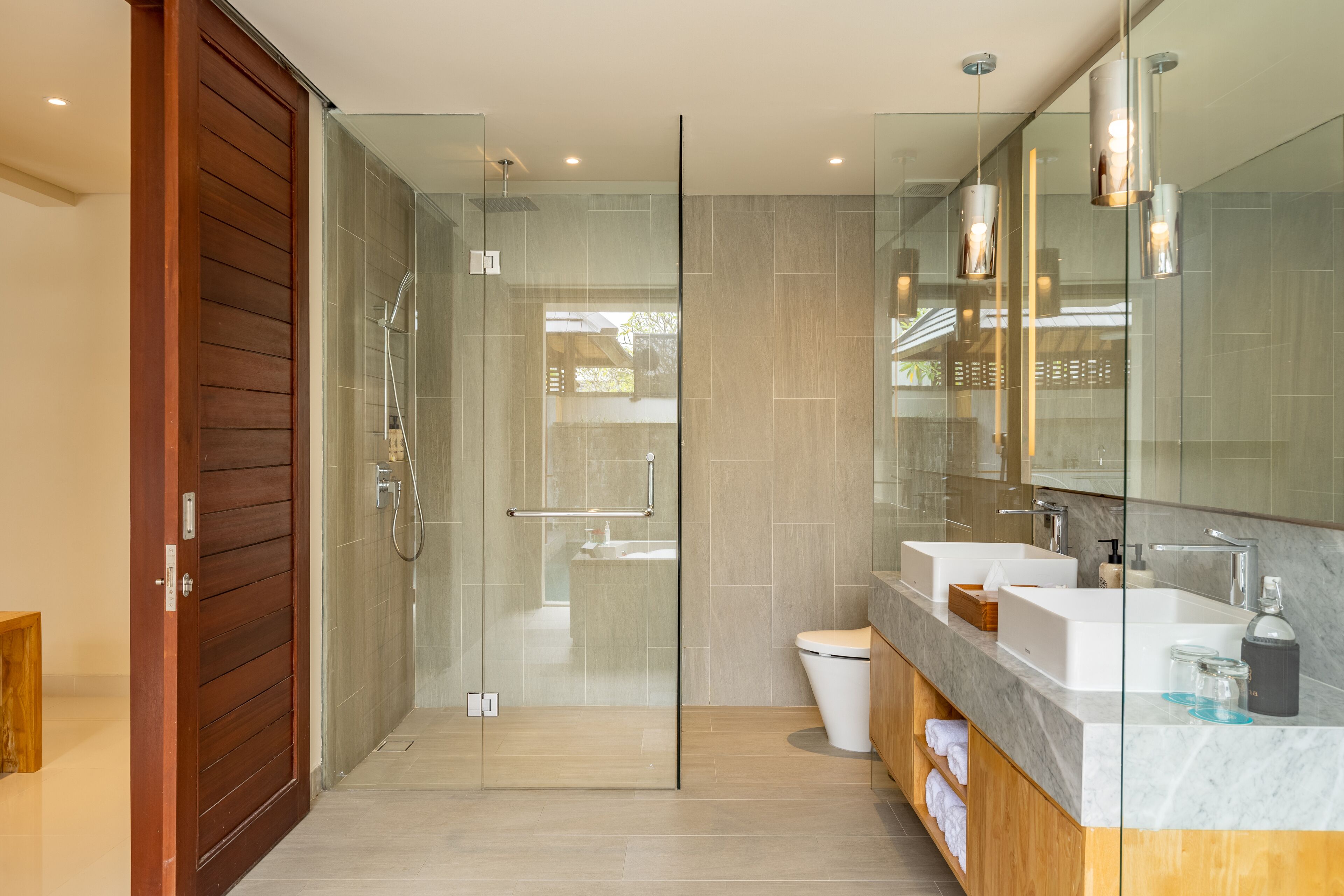 Un baño moderno con ducha acristalada, puerta de madera y tocador de mármol con un espejo grande.