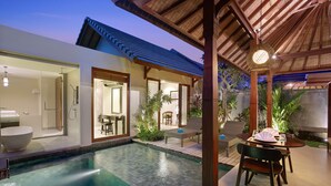 A modern pool area with a covered seating area, a dining table, and a large window overlooking the pool.