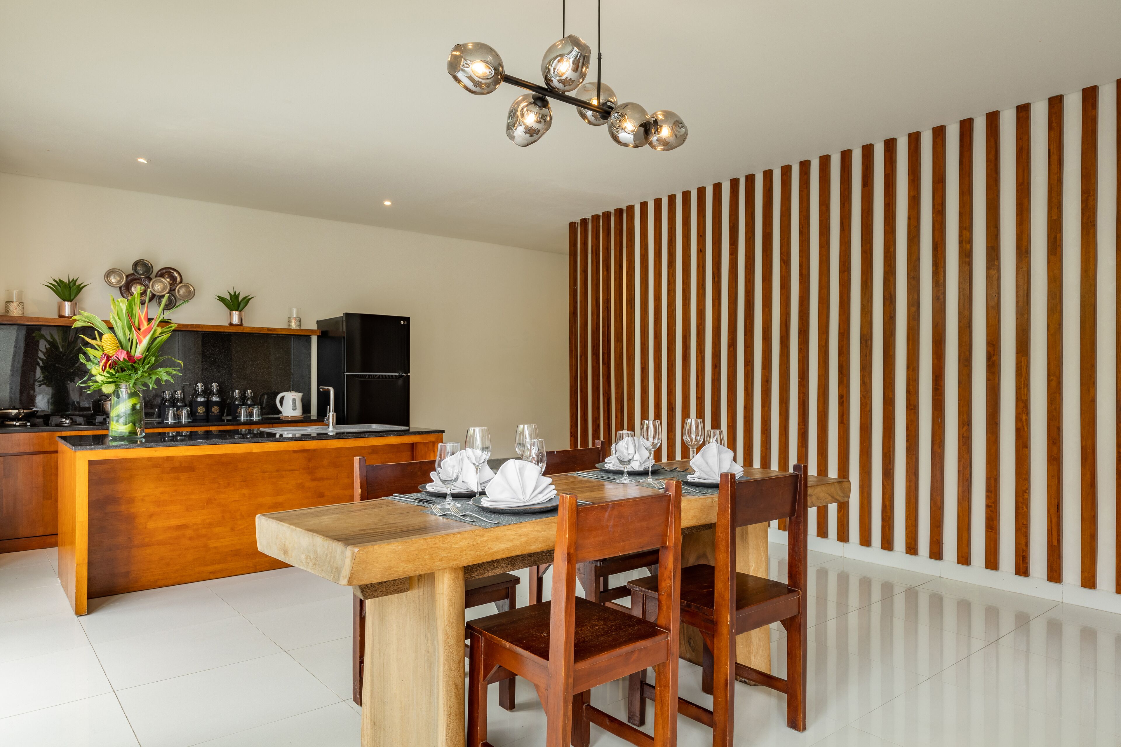 A modern kitchen with a wooden island, a dining table set for four, and a contemporary light fixture.