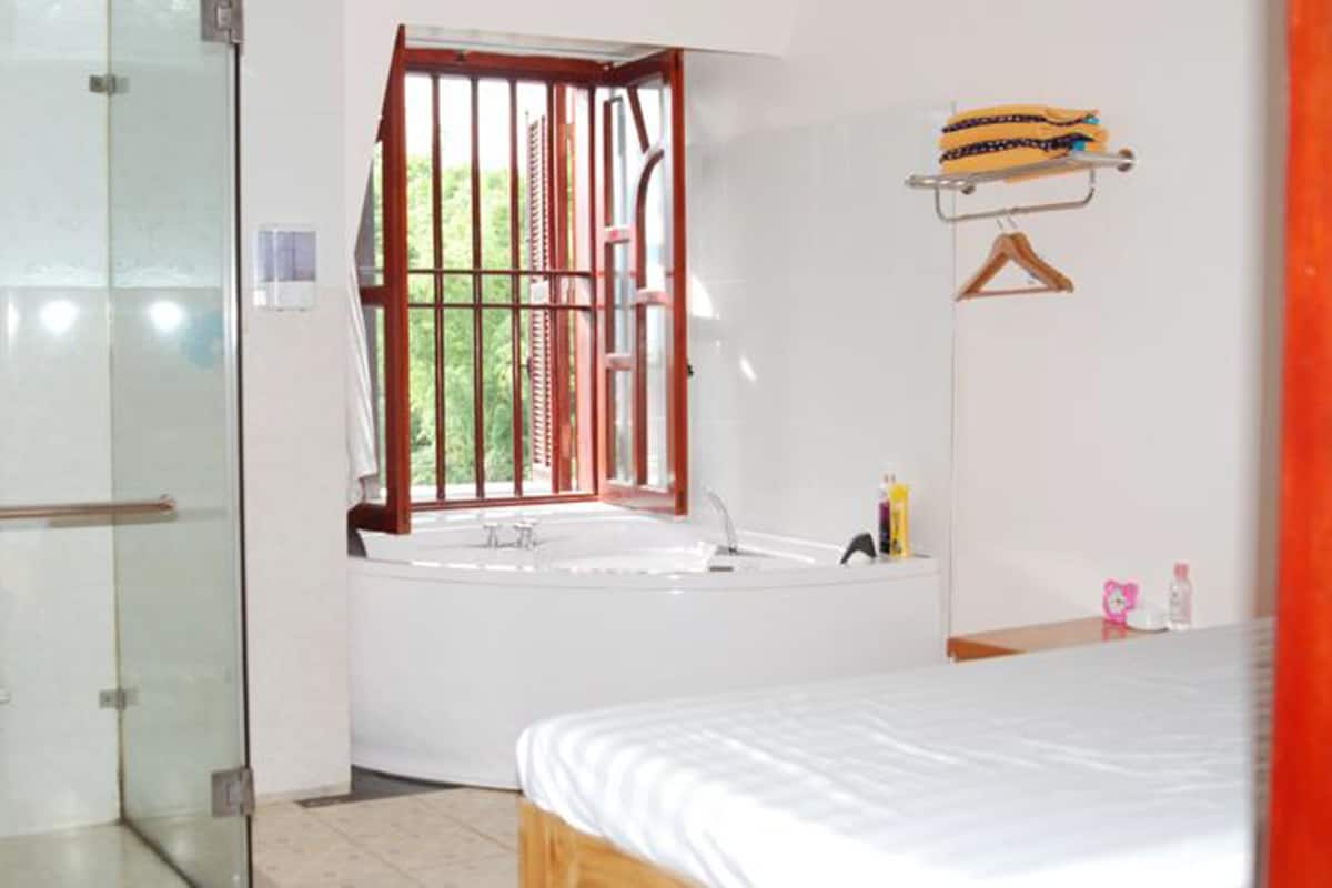 Une salle de bain dotée d’une douche à parois de verre, d’une baignoire et d’une fenêtre donnant sur un espace verdoyant.