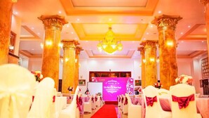 A hotel interior with a red carpet aisle, white chairs with red sashes, and a large chandelier. - A1 Hotel Dien Bien (Dien Bien Phu)