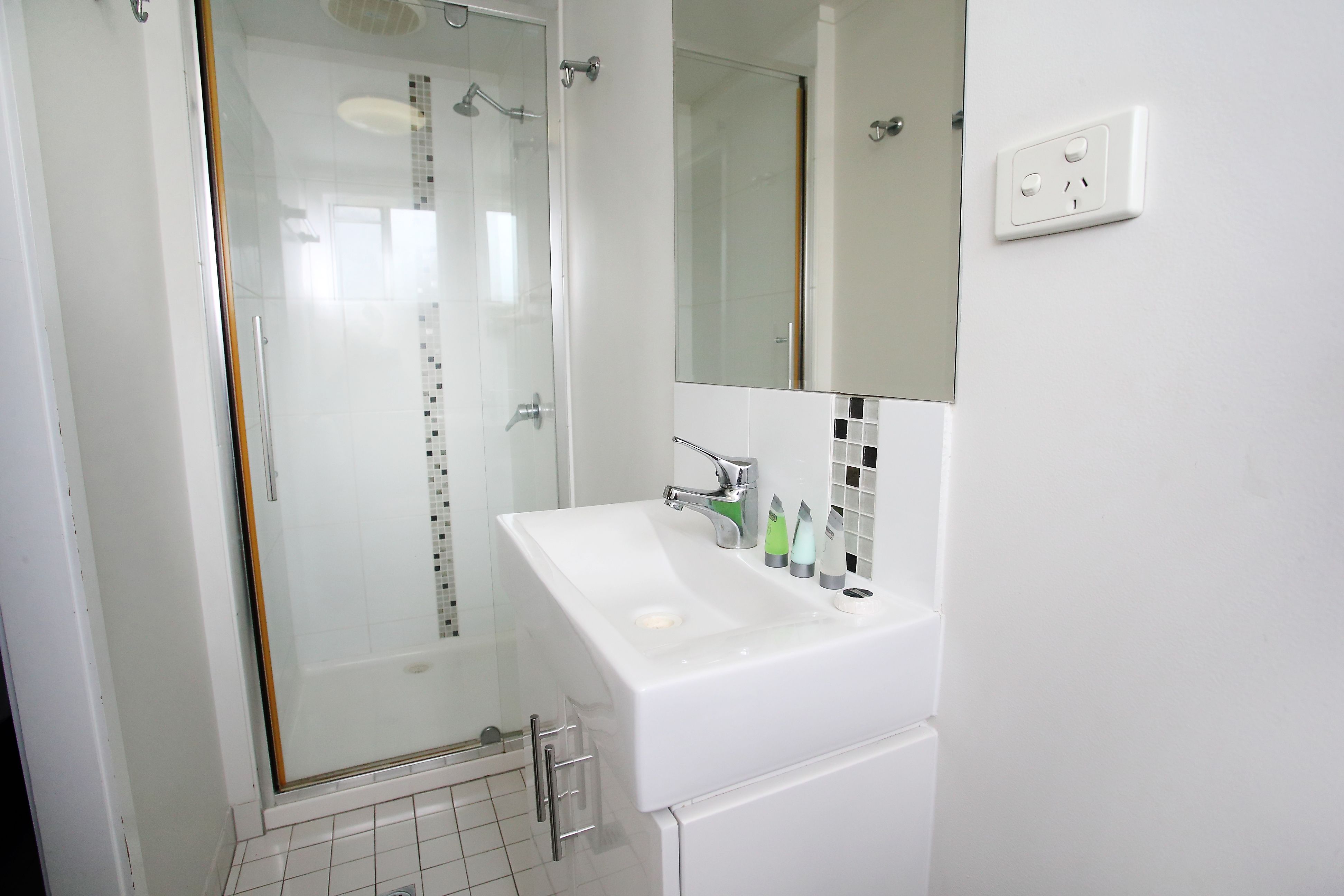 A modern bathroom with a glass-enclosed shower, a white sink with a mirror above it, and a tiled floor.