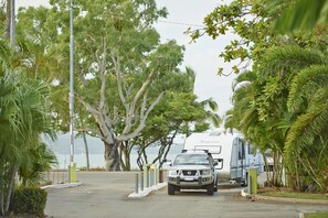 Un estacionamiento con una camioneta y un remolque, rodeado de árboles y vista al océano.
