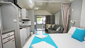 Habitación pequeña con cama, sofá, kitchenette y vista por una puerta.