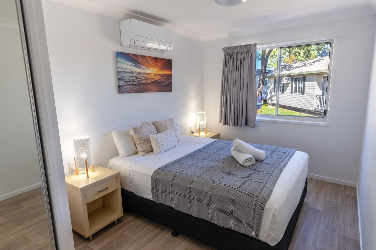 A neatly arranged bedroom with a bed, bedside lamps, a painting, and a window with curtains.