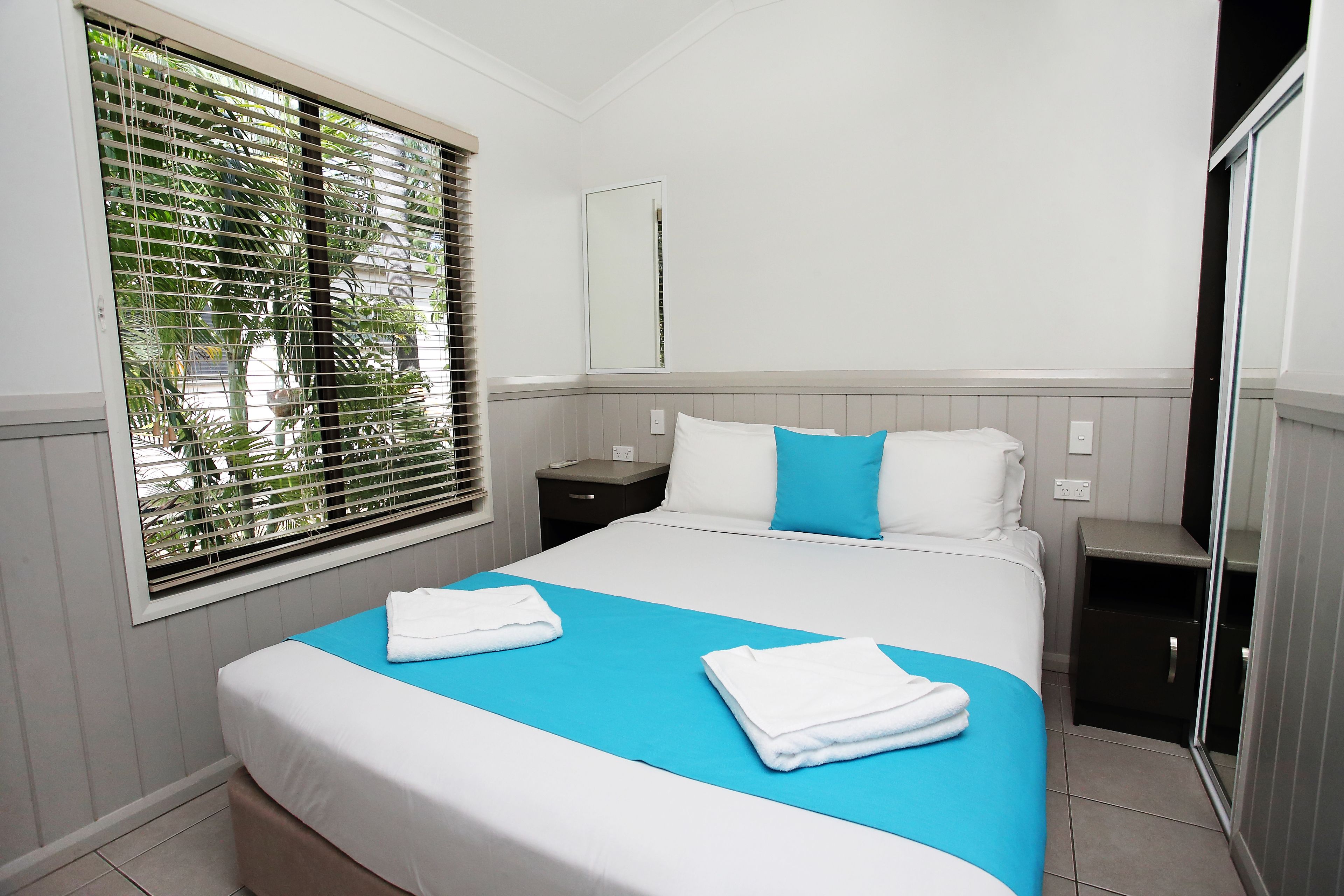 Una habitación de hotel con cama, mesita de noche, espejo y ventana con persianas.