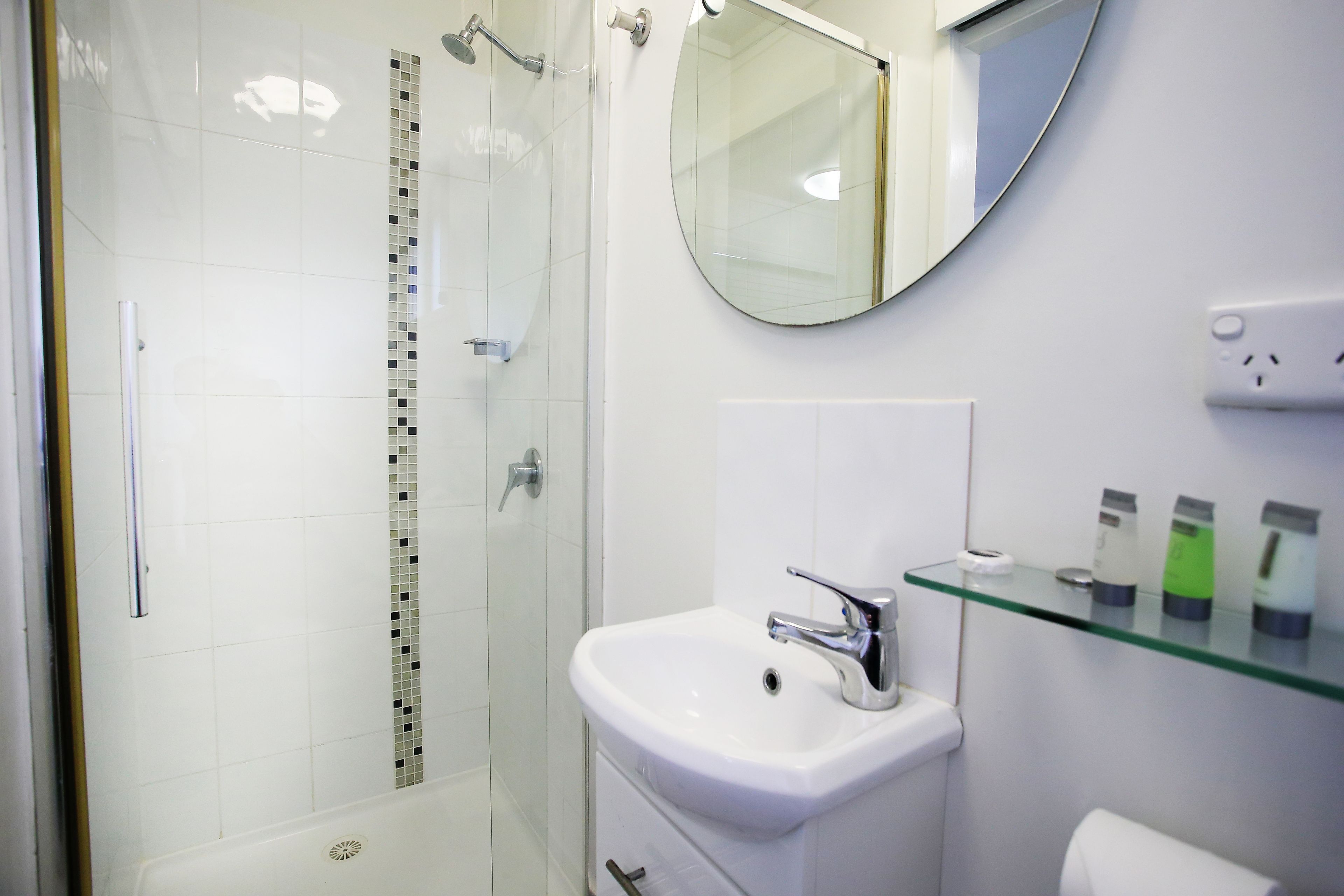 A modern bathroom with a glass shower enclosure, a white sink with chrome fixtures, and a round mirror above it.