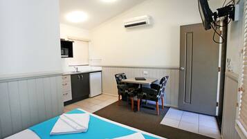 A compact room with a bed, a small kitchenette, a dining table with chairs, and a door.