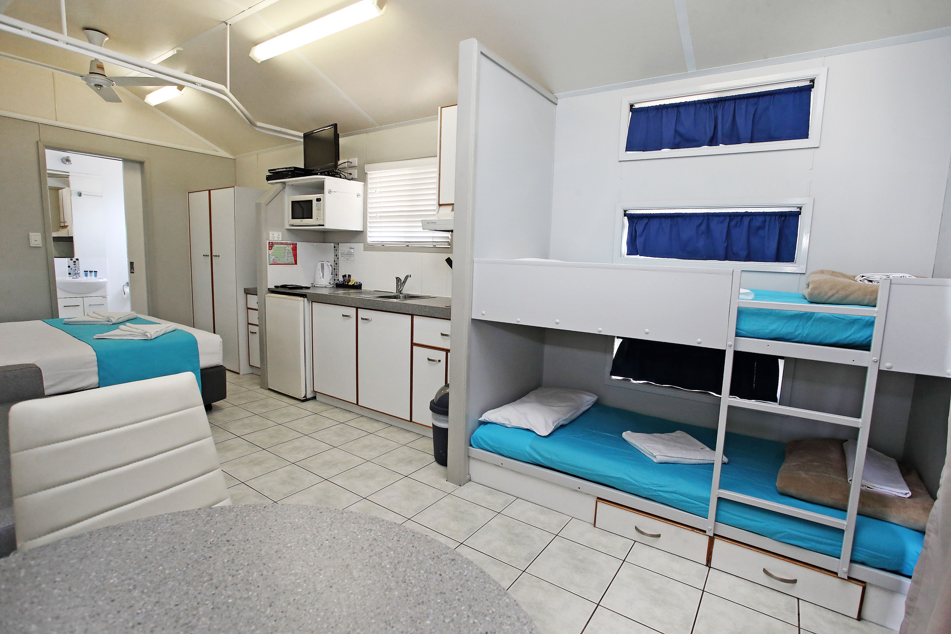 A compact hotel room with bunk beds, a kitchenette, a bathroom, and a small seating area.