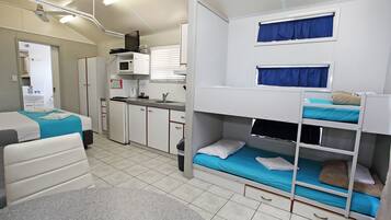 A compact hotel room with bunk beds, a kitchenette, a bathroom, and a small seating area.