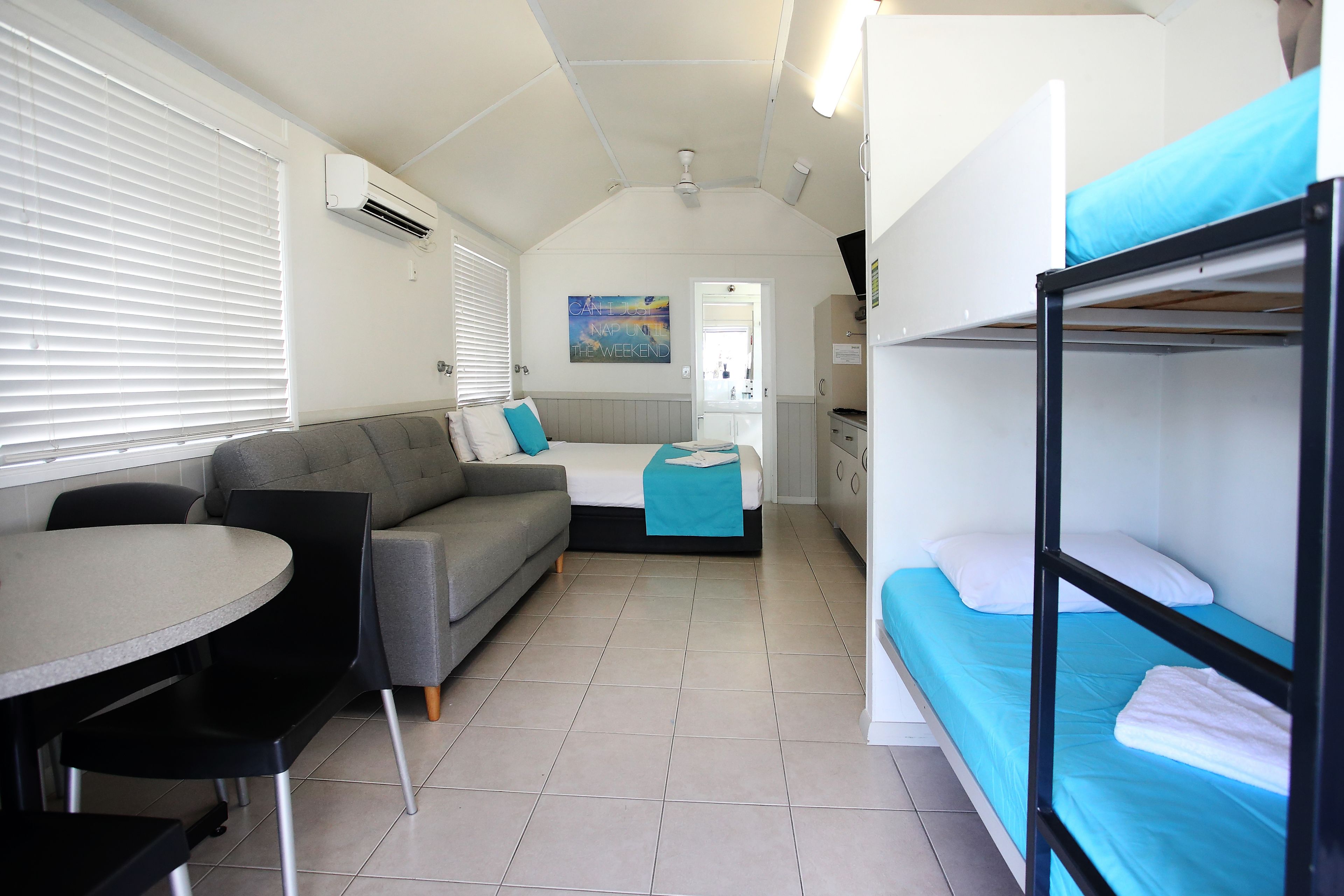 A compact, well-lit room with a sofa, a small table, and bunk beds.