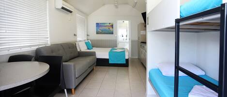 A compact, well-lit room with a sofa, a small table, and bunk beds.