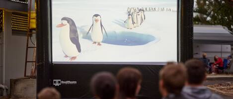 Een groot scherm buiten waarop pinguïns te zien zijn, met een publiek ervoor.