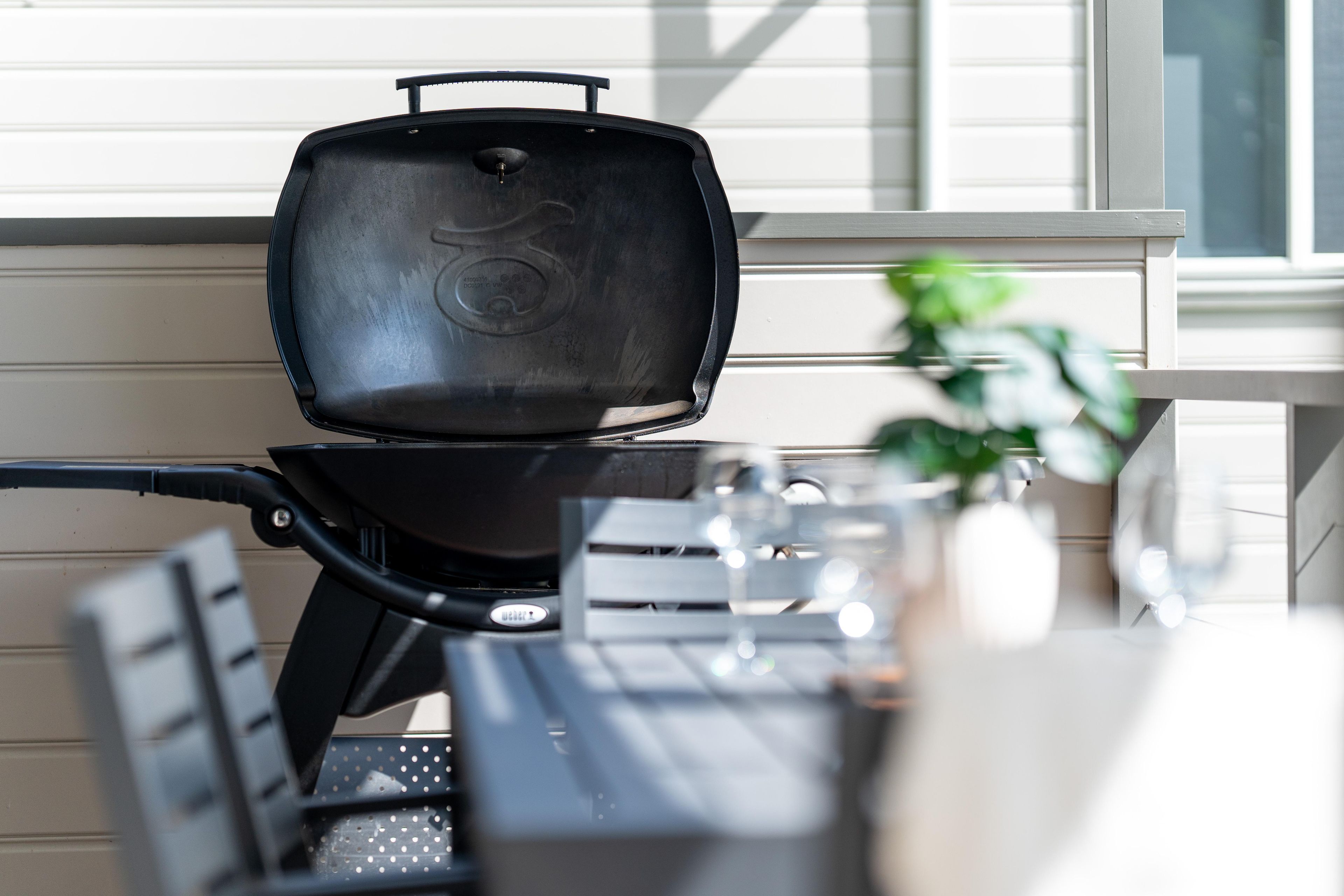 Un barbecue avec couvercle, une table avec des chaises et une plante en pot.