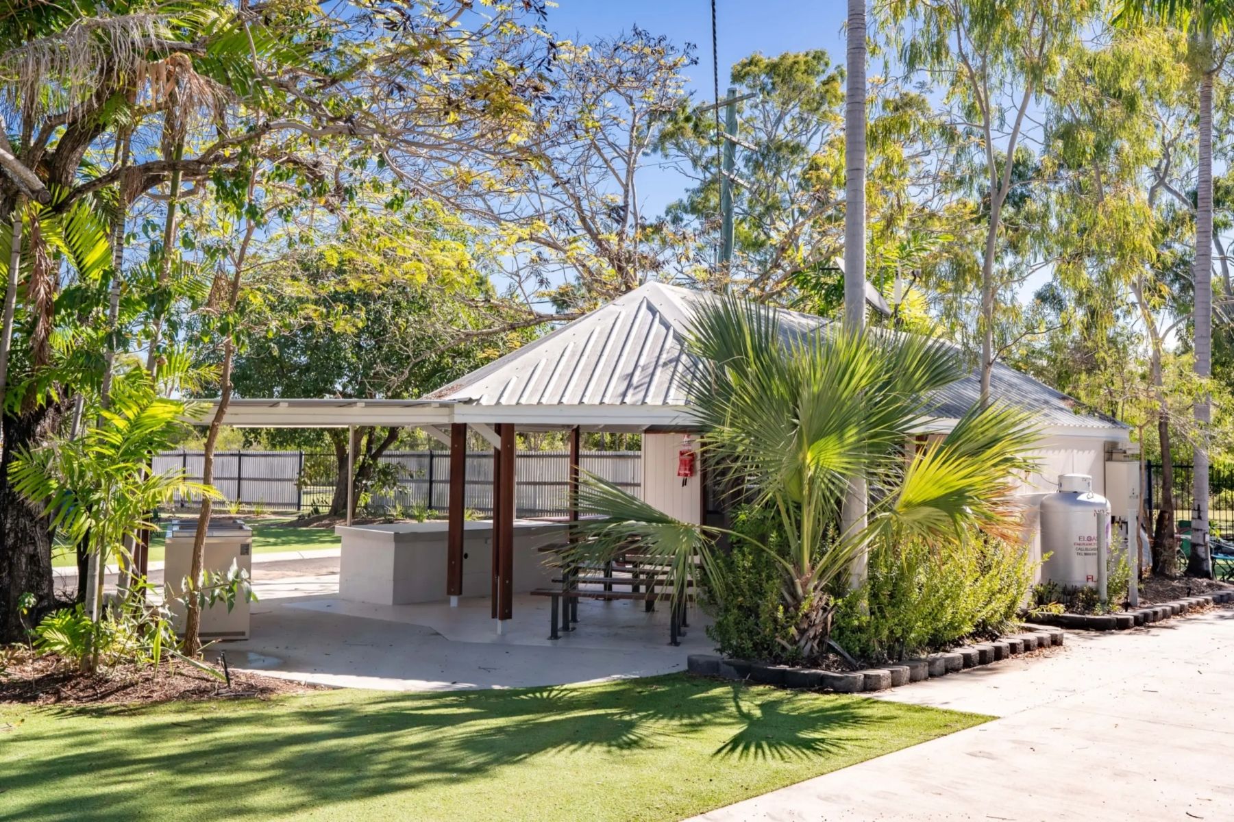 A small building with a covered patio area, surrounded by lush greenery and trees.