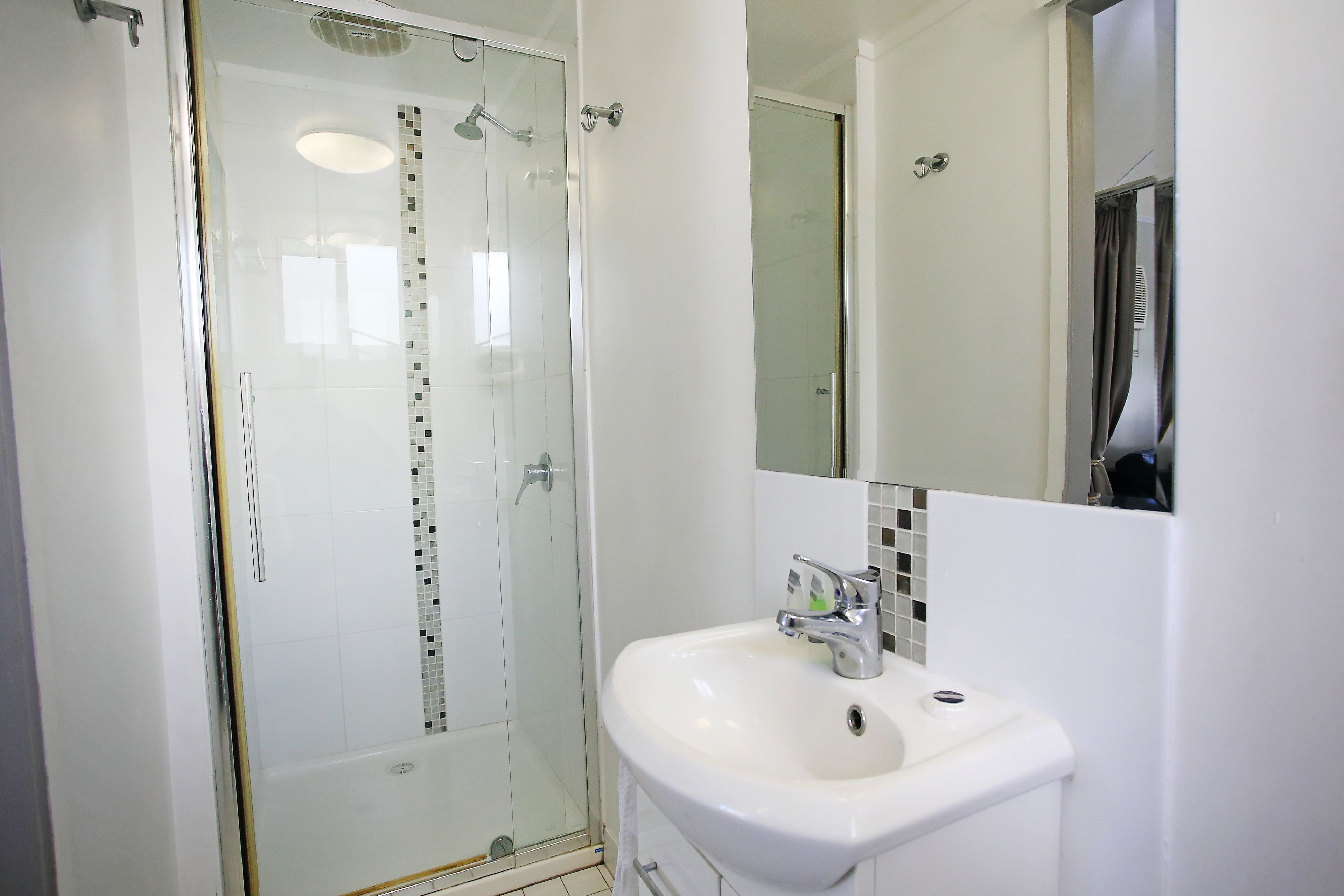 Une salle de bain moderne avec une douche à parois de verre, un lavabo blanc et un miroir au-dessus du lavabo.