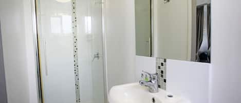 Un baño moderno con ducha de vidrio, lavamanos blanco y espejo sobre el lavamanos.