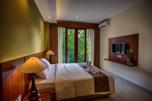 A hotel room with a large bed, a TV mounted on the wall, and a window with a view of trees.