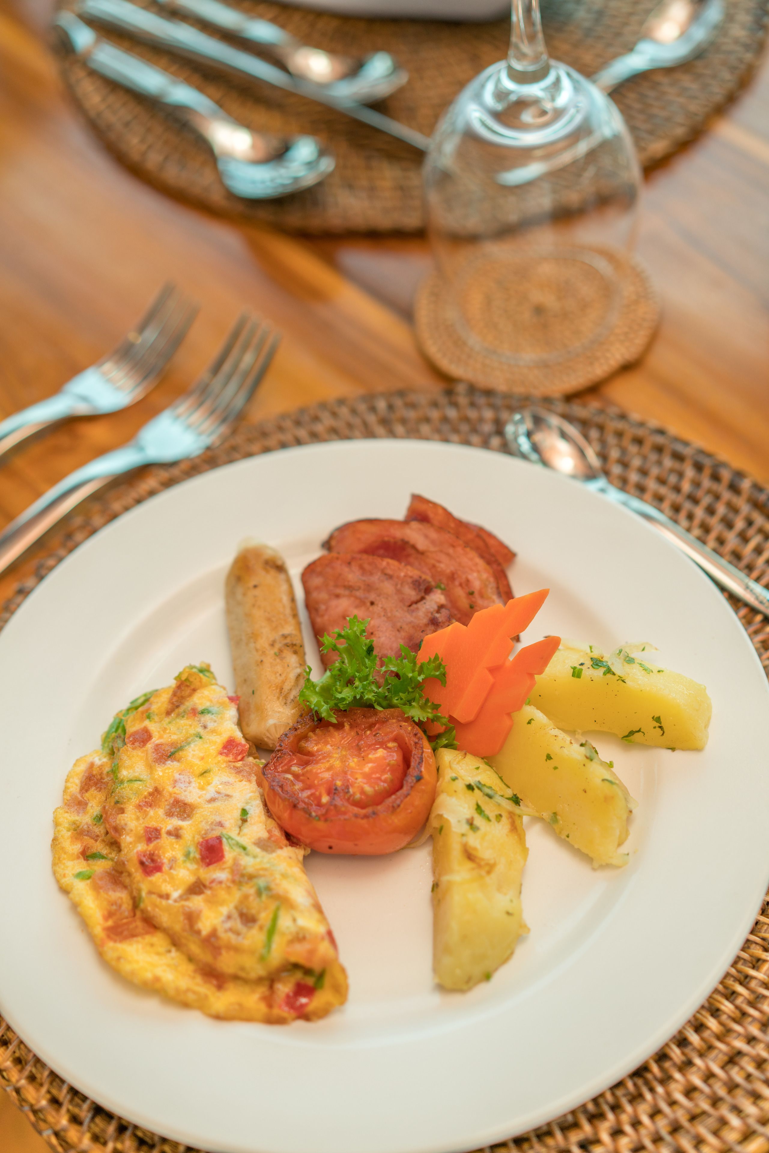 A plate of food including an omelette, sausages, ham, carrots, and potatoes.
