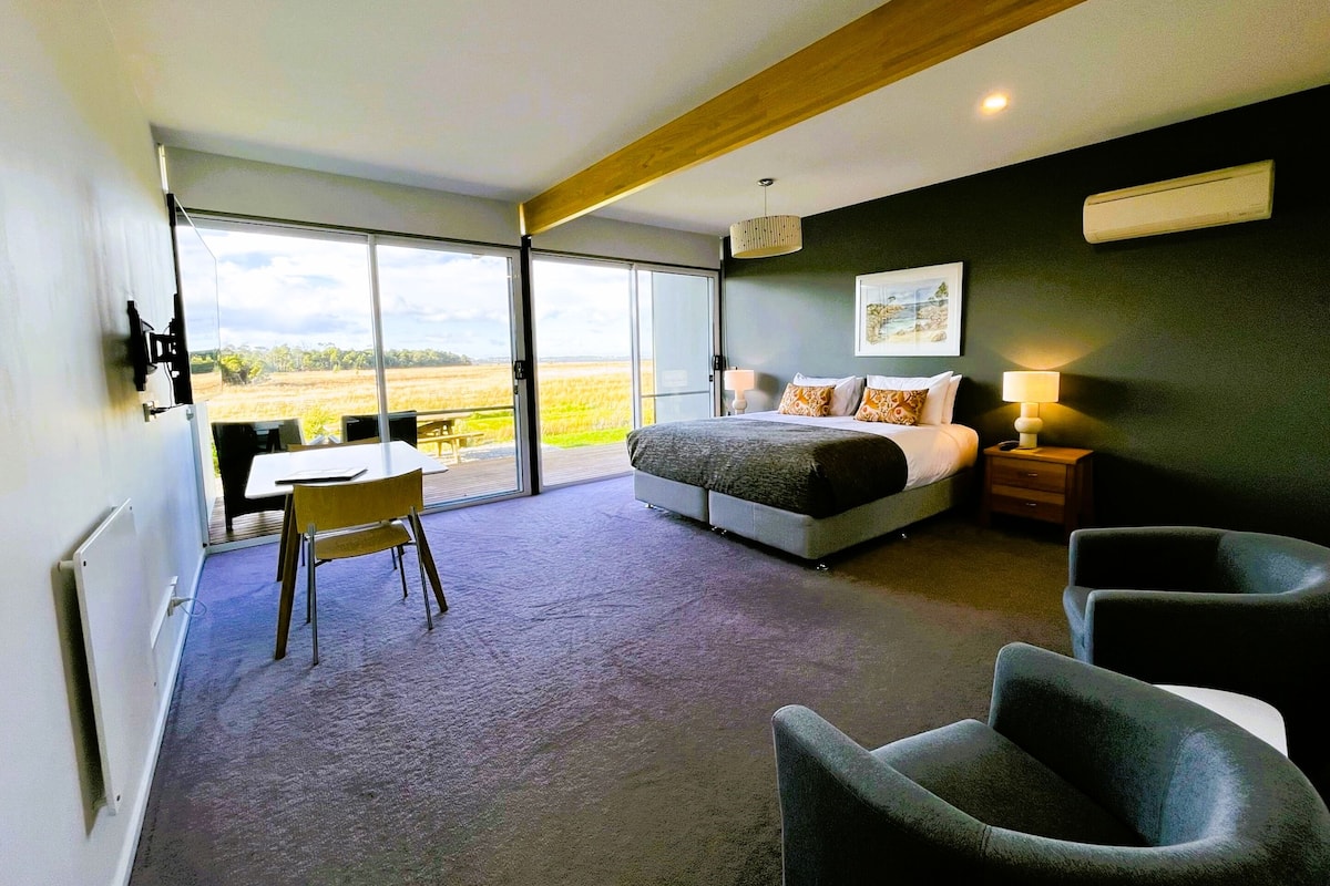 Un dormitorio con cama, escritorio y silla. Hay un ventanal con vistas al exterior.
