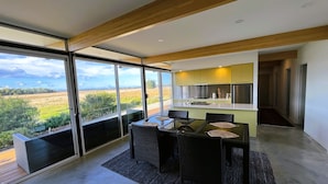 Una cocina moderna con una isla grande, un comedor con muebles de mimbre y vistas a un paisaje rural a través de amplios ventanales correderas.