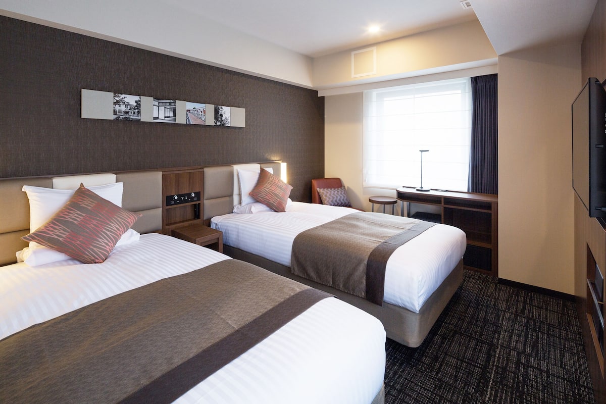 Ein Hotelzimmer mit zwei Betten, einem Schreibtisch, einem Stuhl und einem Fernseher.