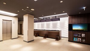 A modern lobby with a reception desk, seating area, and a television screen displaying a scenic view. - Hotel MyStays Yokohama Kannai (Yokohama)