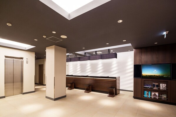 Un hall d’entrée moderne doté d’un comptoir de réception, d’un espace salon et d’un écran de télévision diffusant des images d’un paysage pittoresque.