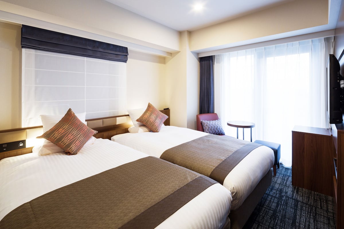 Ein Hotelzimmer mit zwei Betten, einem Schreibtisch, einem Sessel und einem Fernseher.