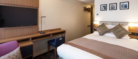 A hotel room with a bed, a desk, a chair, a flat-screen TV, and a wall-mounted air conditioner.