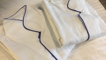 Neatly folded white shirts with blue piping on a bed.