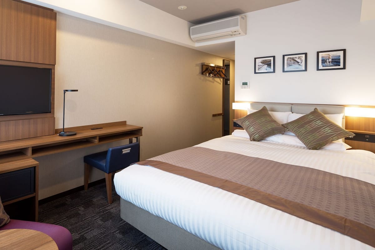 Ein Hotelzimmer mit Bett, Schreibtisch, Stuhl, Fernseher und Wandbildern.