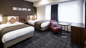 A hotel room with two beds, a small round table, a red chair, and a large window with curtains.