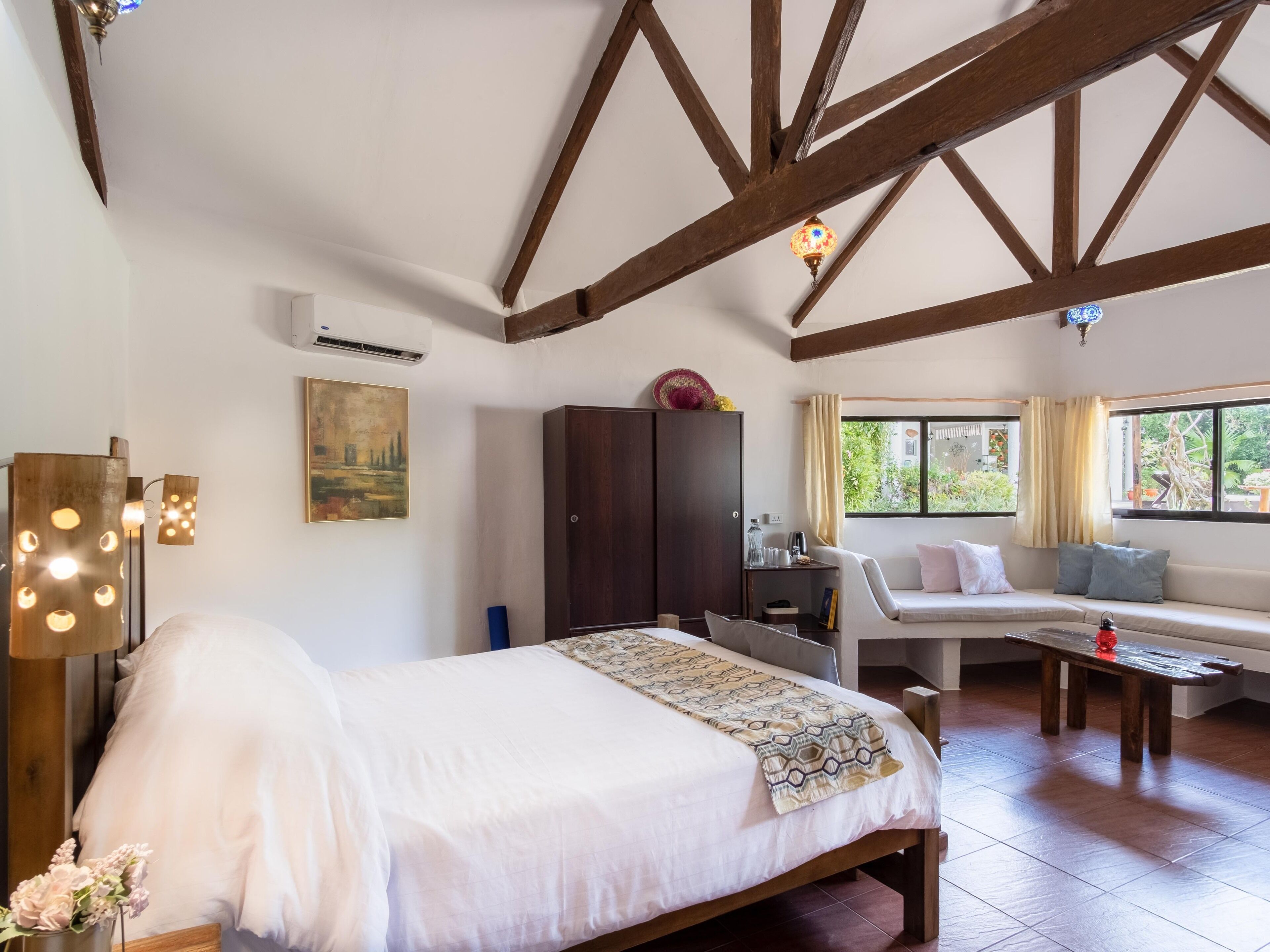 A bedroom with a bed, a wardrobe, a desk, and a seating area with a view of greenery outside.