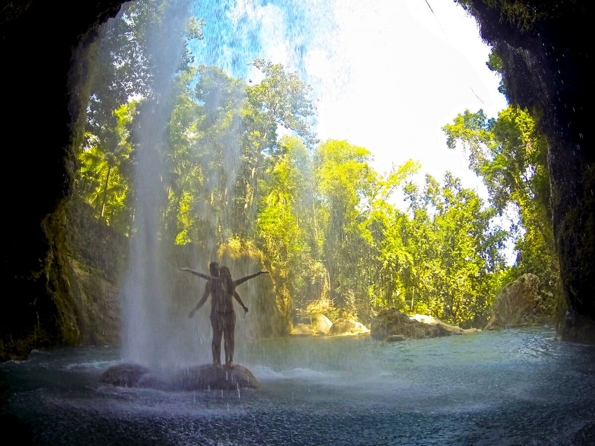 Una persona de pie sobre una roca en una cueva, con una cascada al fondo.