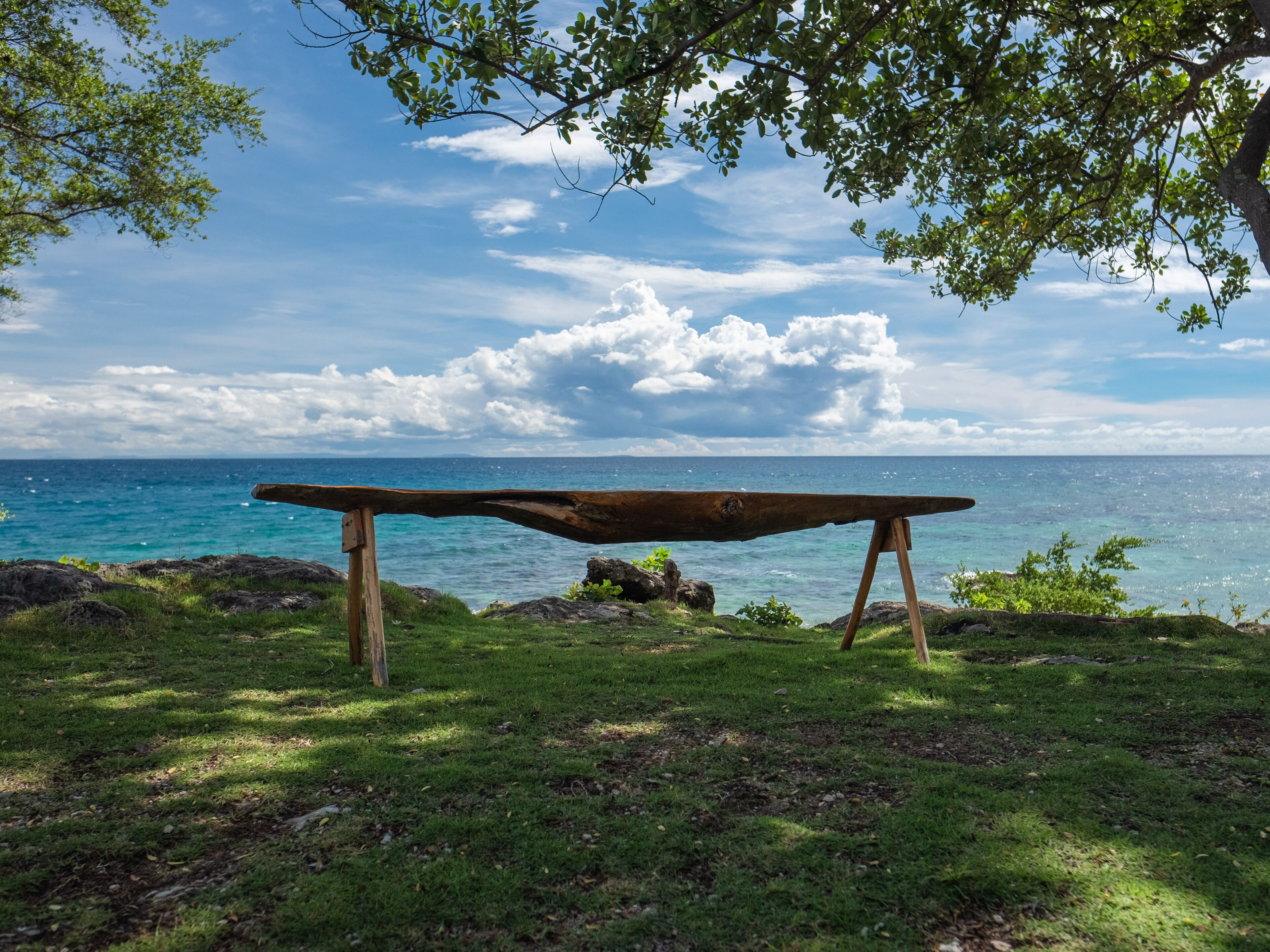 A wooden bench on a grassy area overlooking a body of water with a clear sky.