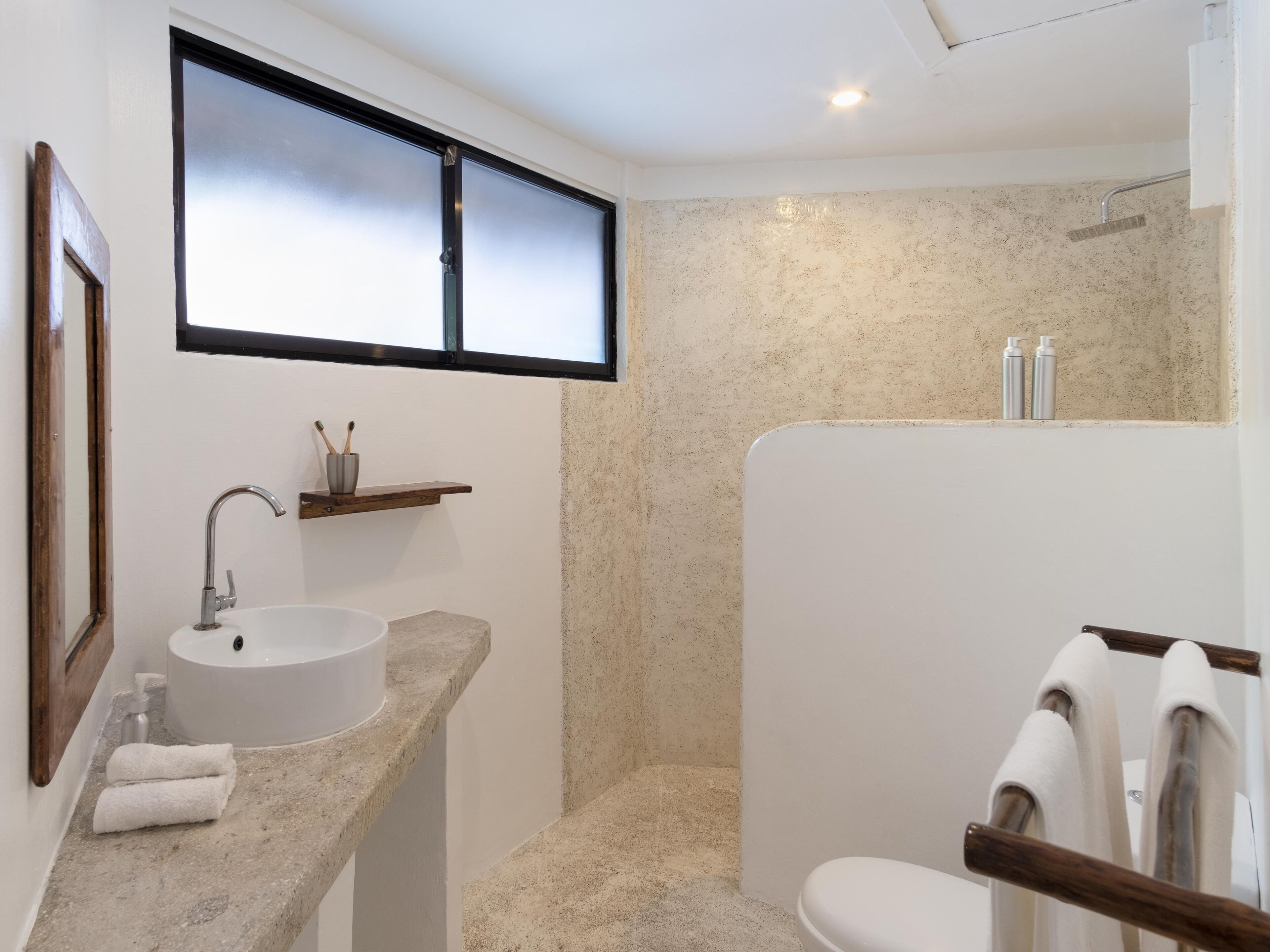 Un baño con lavamanos, espejo, toallero, ducha y ventana.