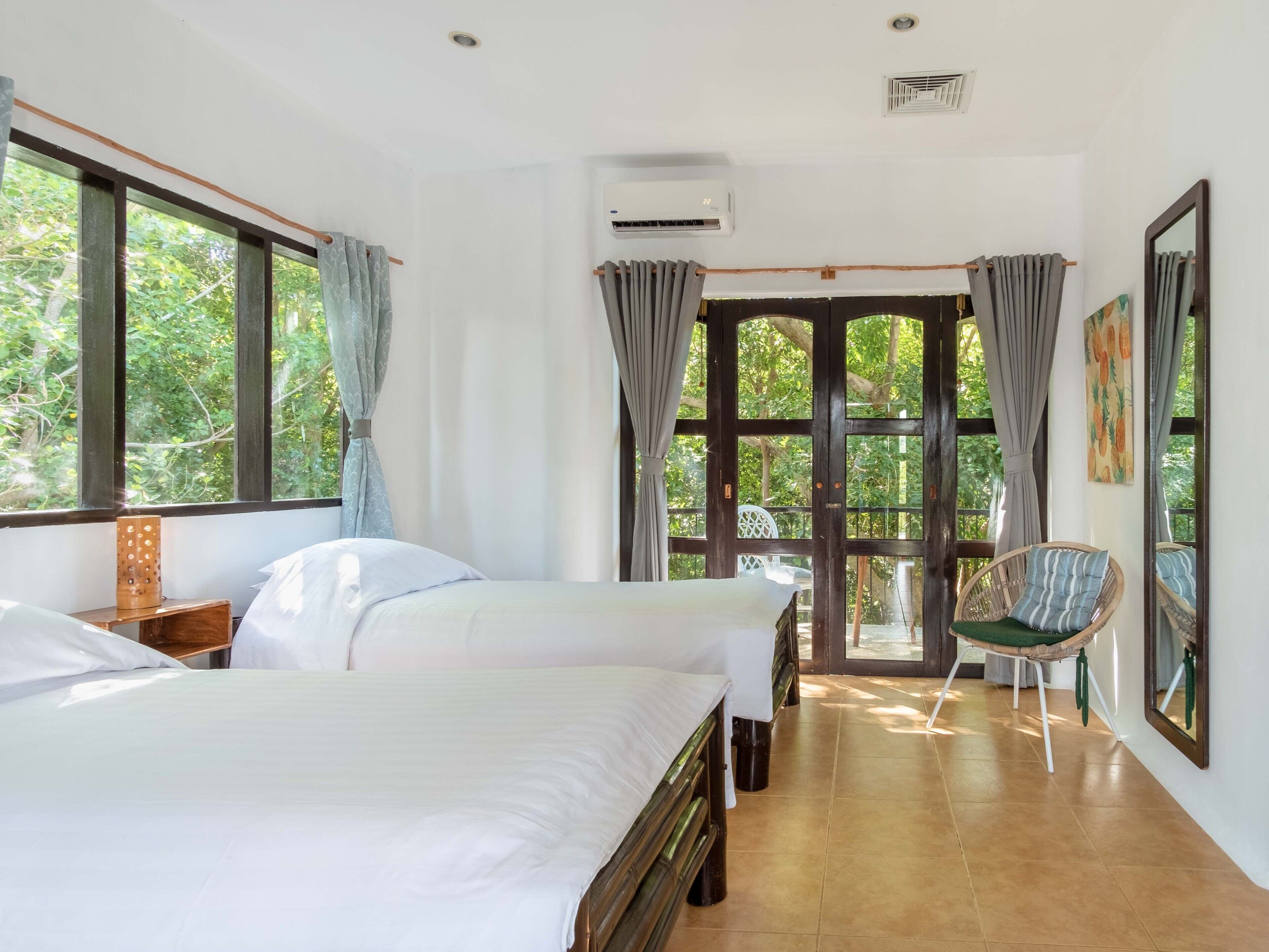A bedroom with two beds, a chair, a window, and a door leading to a balcony.