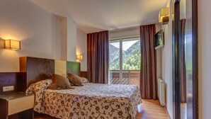 A bedroom with a bed, a nightstand, a TV, and a view of mountains through the window.