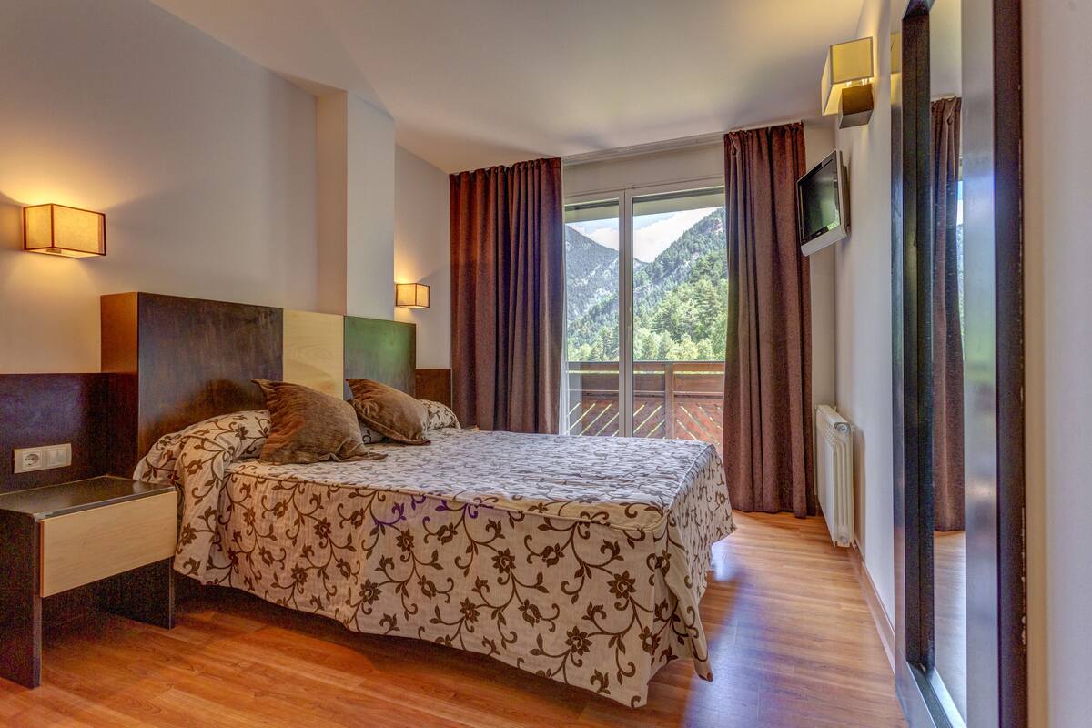 Une chambre à coucher avec un lit, une table de chevet, un téléviseur et une vue sur les montagnes par la fenêtre.