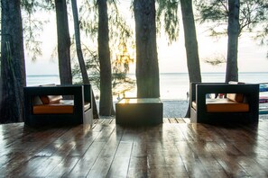A wooden deck with two wicker chairs and a table, overlooking a beach and ocean.